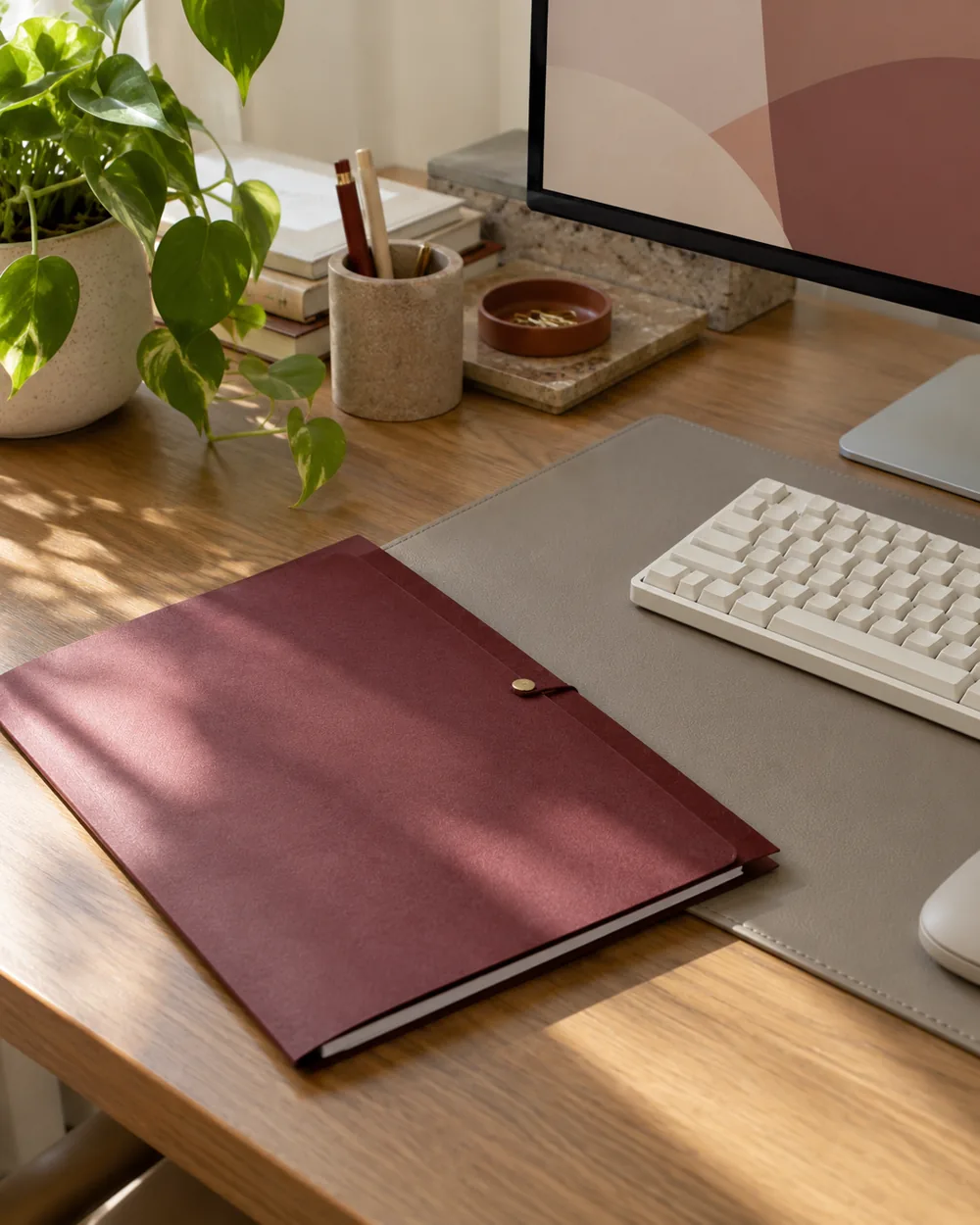 muted burgundy folder beside warm gray desk mat and plain keyboard